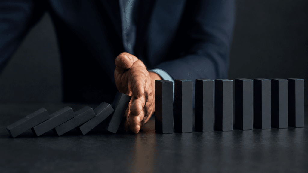 A hand stopping falling dominoes, symbolising structured control over marketing risk in complex B2B sales.
