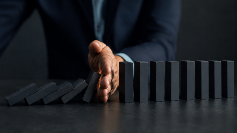 A hand stopping falling dominoes, symbolising structured control over marketing risk in complex B2B sales.