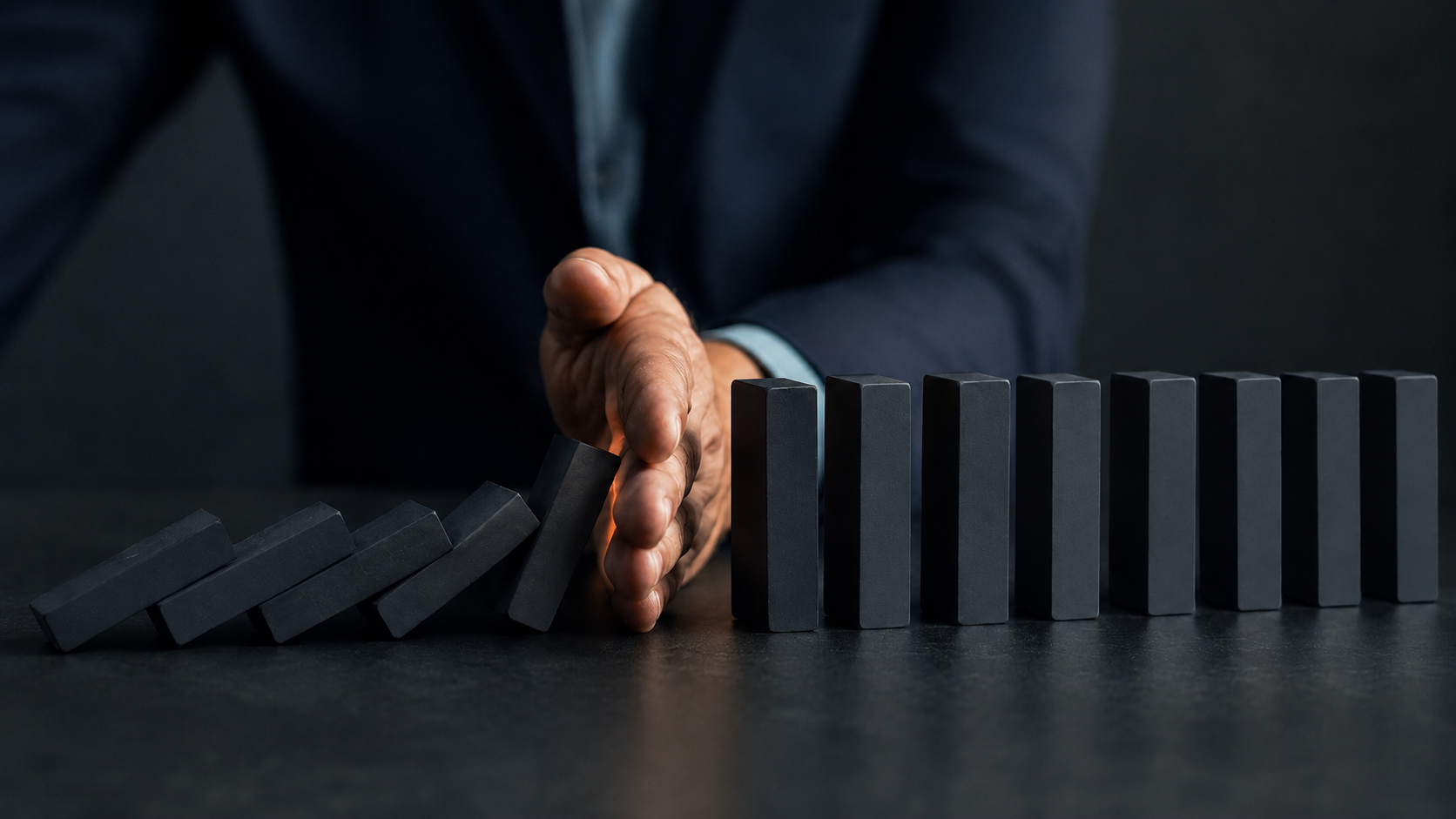 A hand stopping falling dominoes, symbolising structured control over marketing risk in complex B2B sales.
